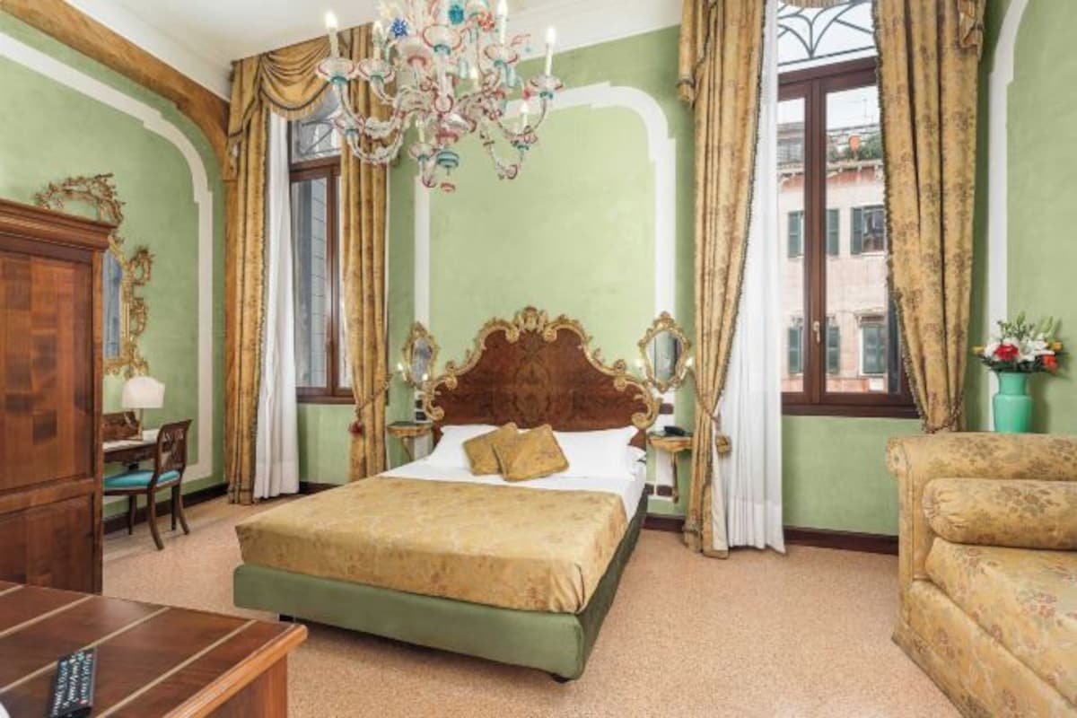 A room with a large bed, a wooden dresser, a chair, a desk, and a chandelier.