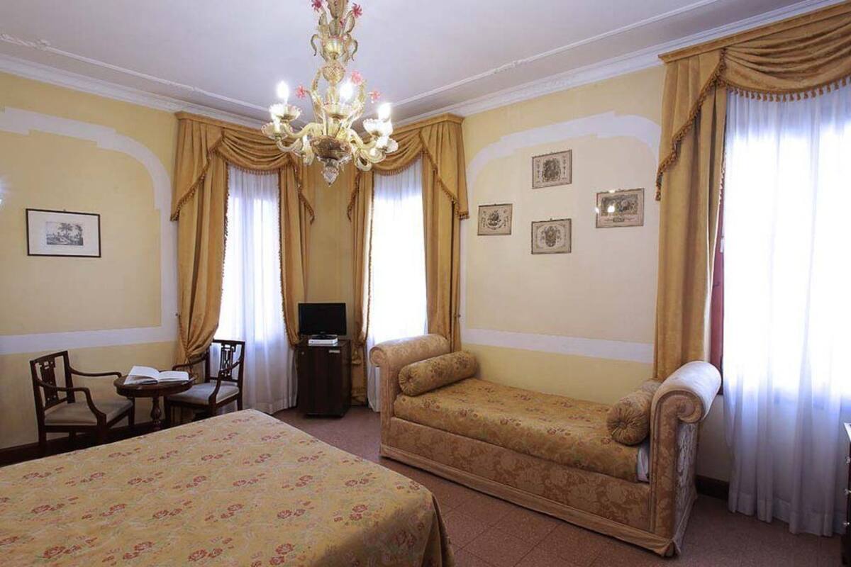 A hotel room with two beds, a sofa, a TV, and a chandelier.