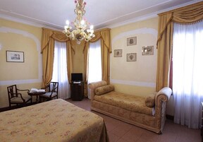 Camera d'albergo con due letti, un divano, una TV e un lampadario.
