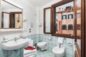 Uma casa de banho com duas pias, sanita e bidé. Há uma janela com vista para edifícios.