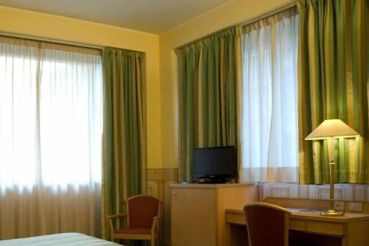 A hotel room with a bed, two chairs, a desk with a television, and curtains.