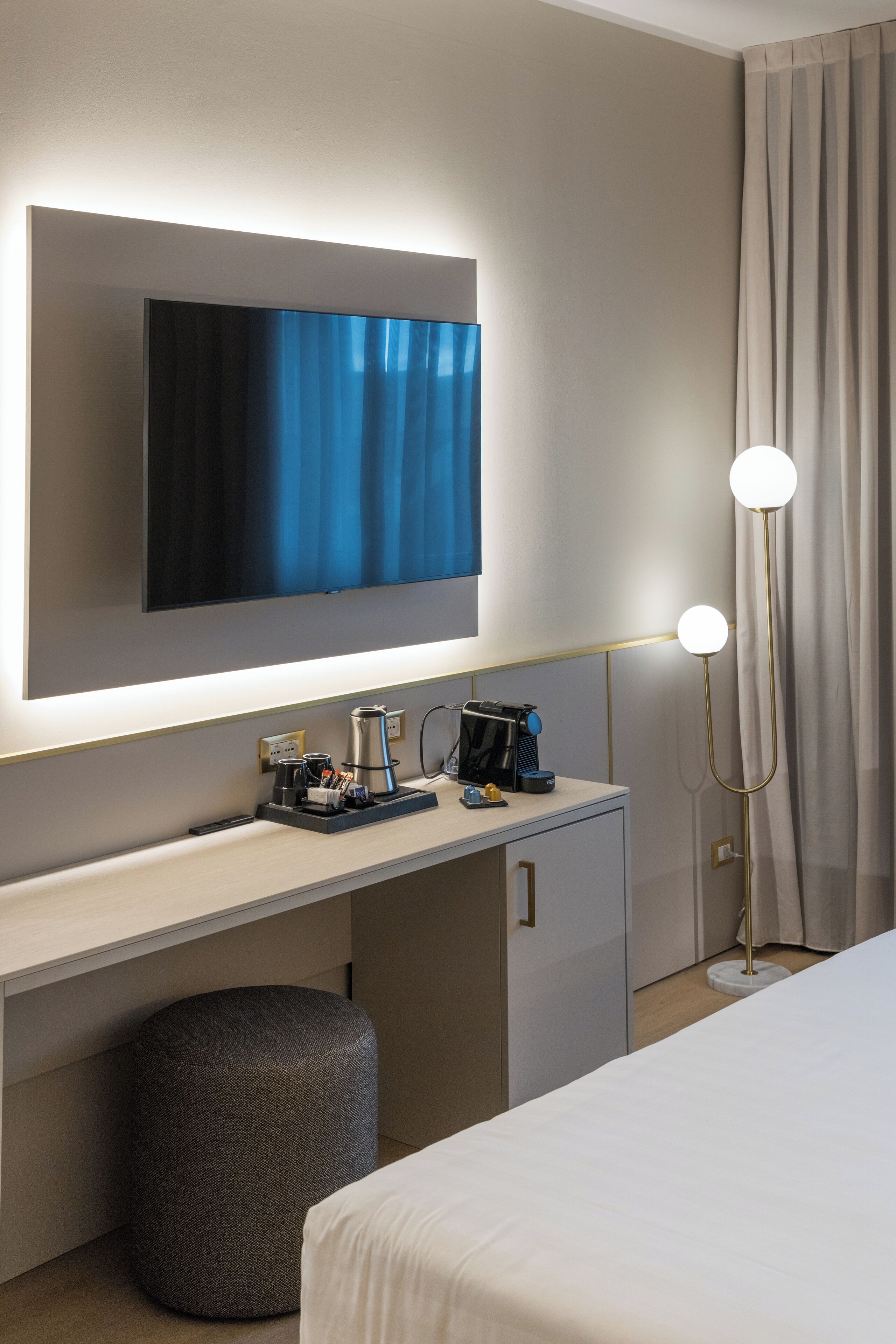 Een hotelkamer met een bed, een bureau met een flatscreen televisie, een koffiezetapparaat en een vloerlamp.