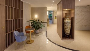 Un hall d’entrée moderne avec un mur lambrissé en bois, un fauteuil bleu, une petite table ronde, une plante en pot et un vase décoratif.