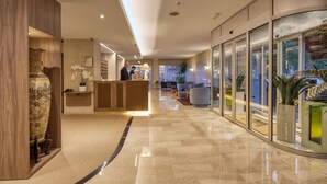 Un hall d’hôtel moderne avec un comptoir d’accueil, un espace salon et de grandes fenêtres.