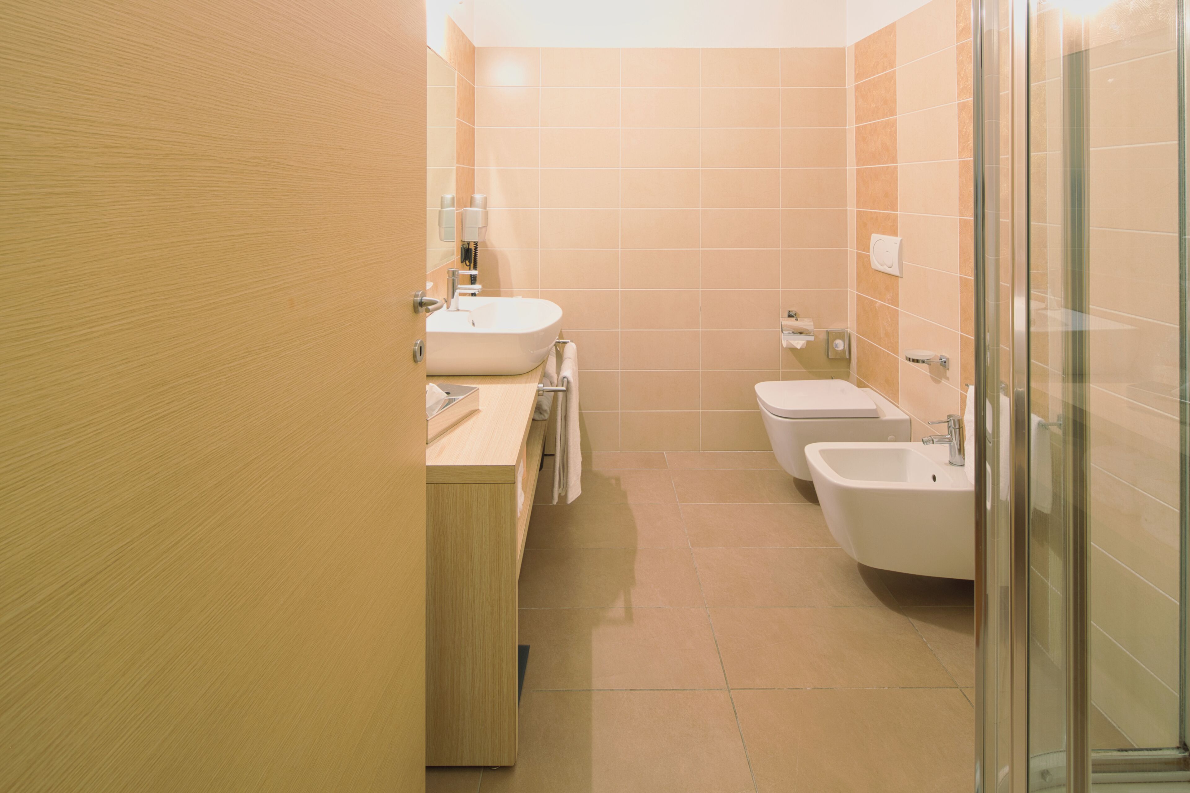 Une salle de bain moderne avec un meuble-lavabo en bois, un lavabo, un bidet et une douche à parois de verre.