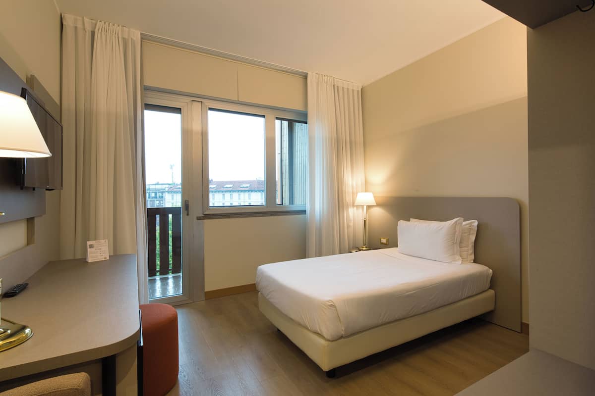 A hotel room with a bed, a desk, a chair, a TV, and a window with curtains.