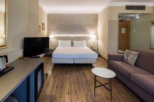 A hotel room with a bed, a TV, a sofa, a small table, and a coffee machine.