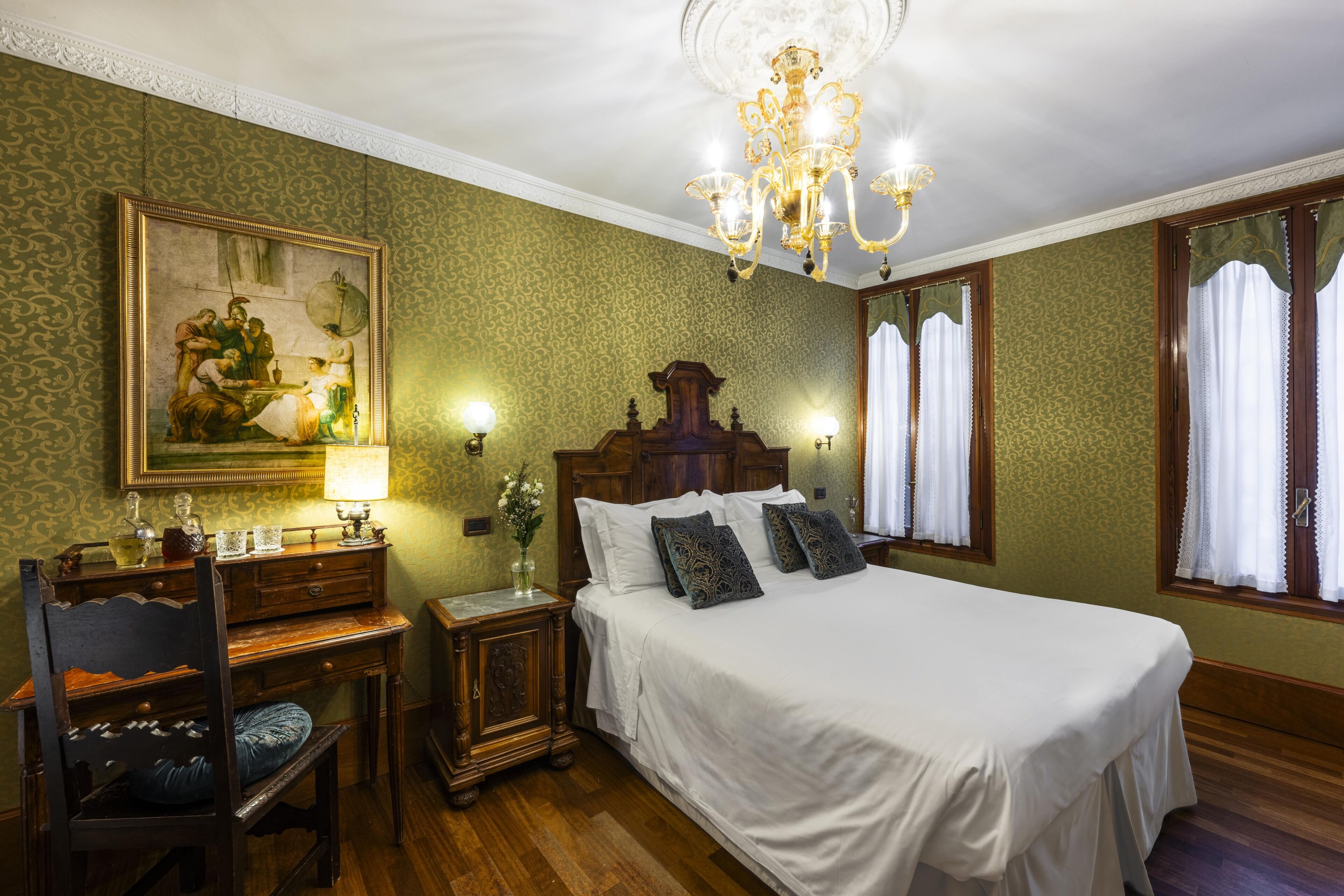 A classic bedroom with a large bed, a wooden nightstand, a desk, and a chair.
