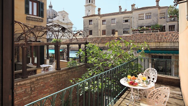 Ein Balkon mit gedecktem Tisch für das Frühstück, mit Blick auf eine Stadtlandschaft mit historischen Gebäuden und einem Turm.