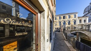 Eine enge Straße mit einem historischen Gebäude, das ein großes Fenster mit der Inschrift 'Casa Nico Polo Anno 1848' zeigt.