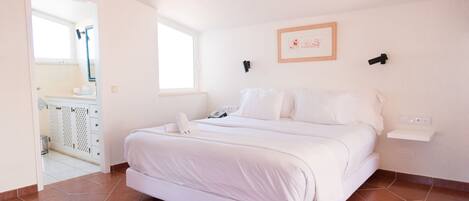 A bedroom with a bed, a window, a wall-mounted shelf, and a door leading to a bathroom.