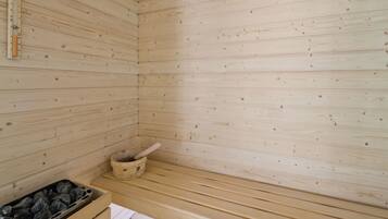 A sauna with wooden walls and benches, a wooden bucket, and a container of stones.