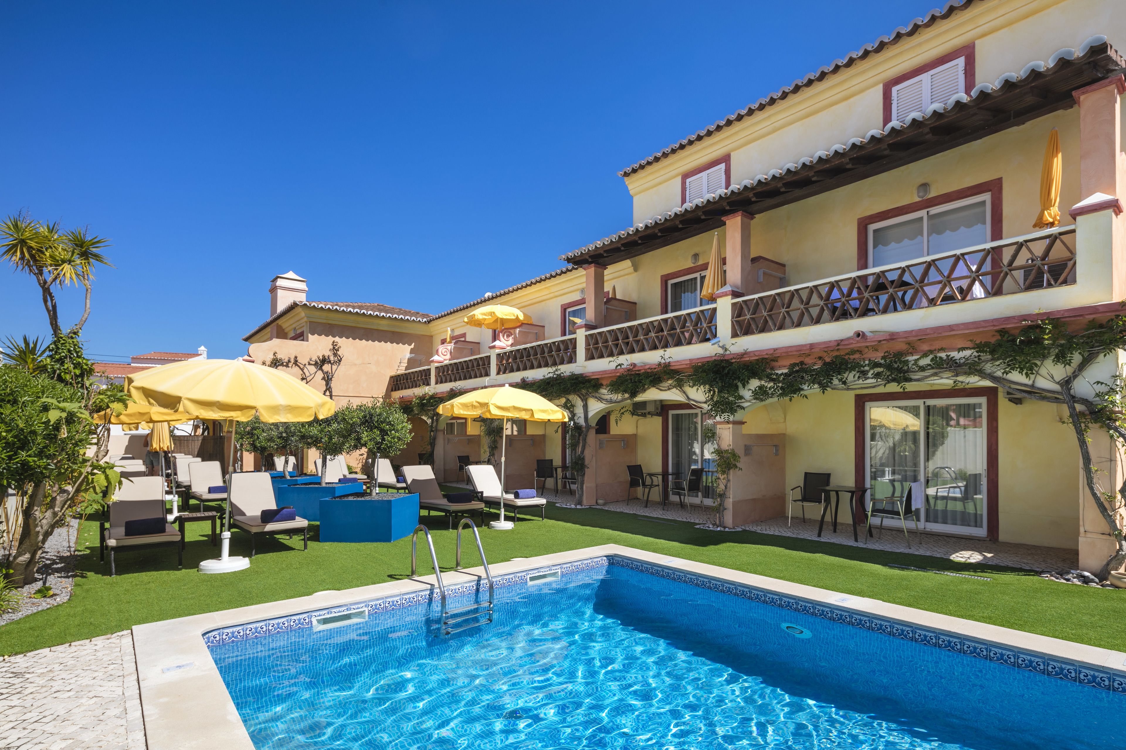 A hotel with a swimming pool, outdoor seating, and a balcony with umbrellas.