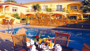 A poolside breakfast setup with a table, chairs, and a fruit basket. - Costa D’Oiro Ambiance Village (Lagos)