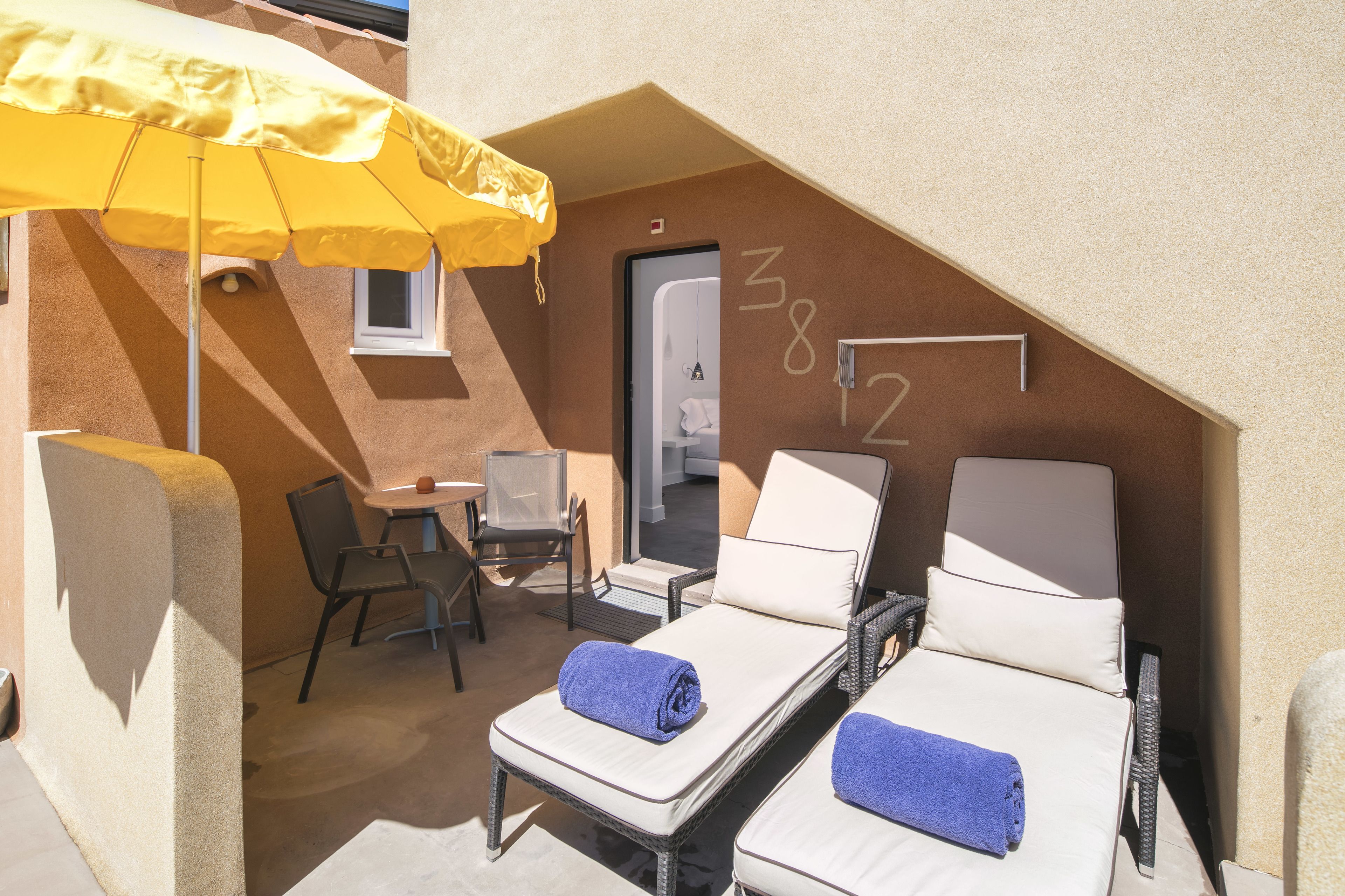 A small, private balcony with two sun loungers, a yellow umbrella, a small table, and a chair.