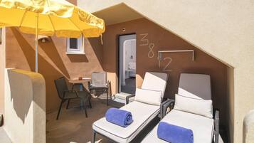 A small, private balcony with two sun loungers, a yellow umbrella, a small table, and a chair.