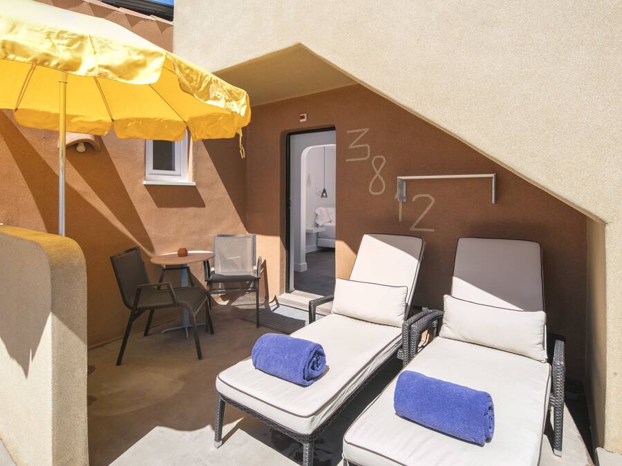 A small, private balcony with two sun loungers, a yellow umbrella, a small table, and a chair.