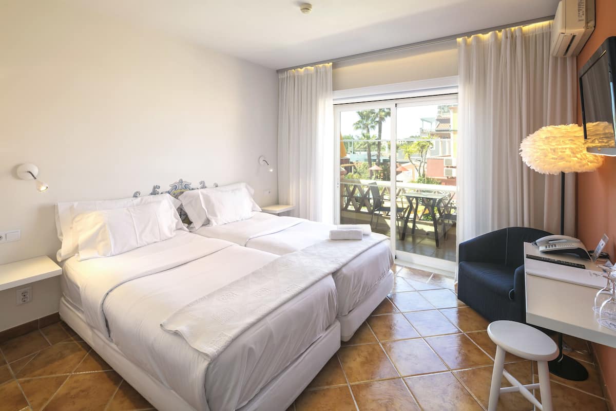 A hotel room with a large bed, a desk with a chair, a window with curtains, and a view of the outside.