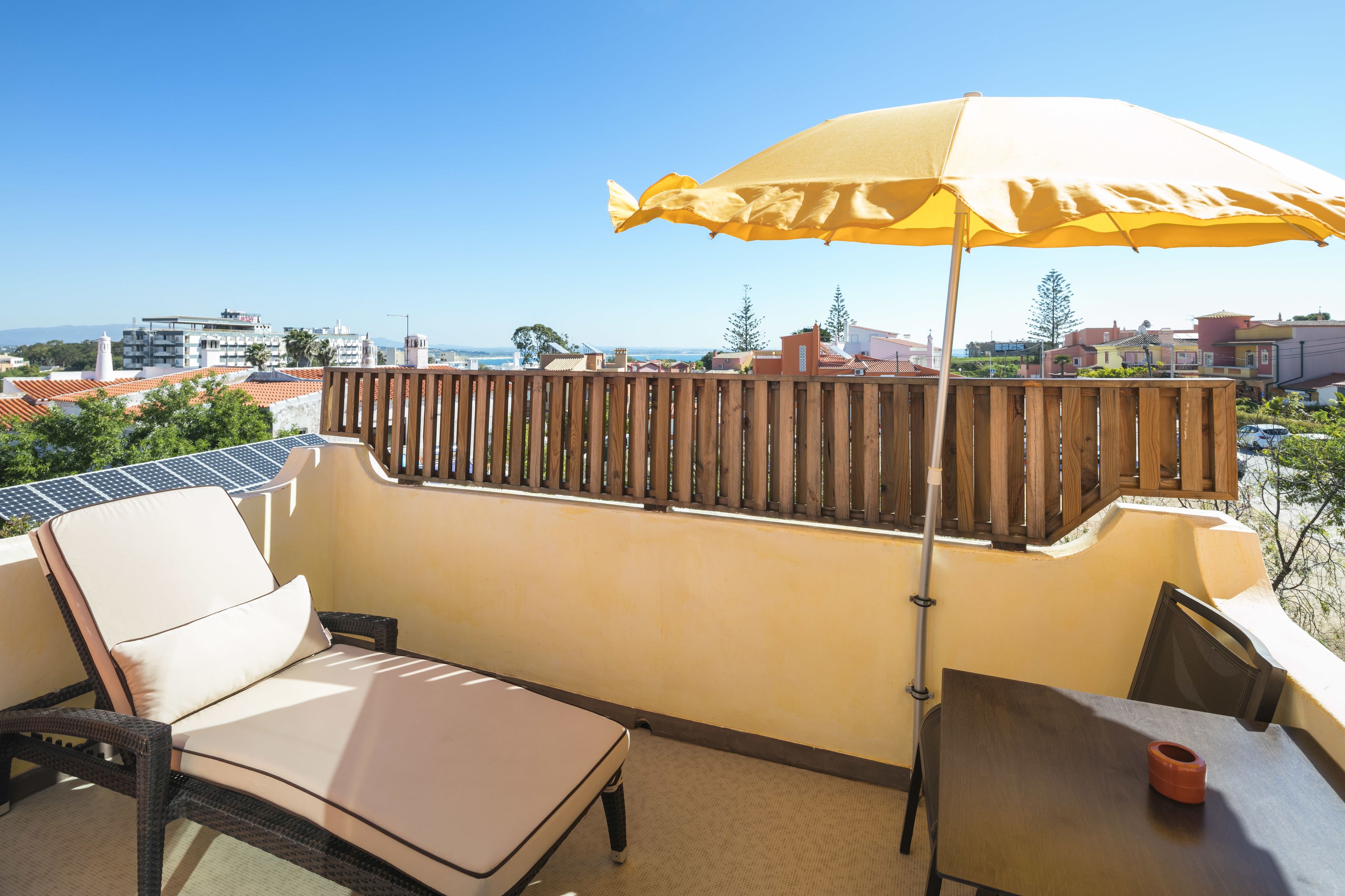 A balcony with a yellow umbrella, a table, and a chair.