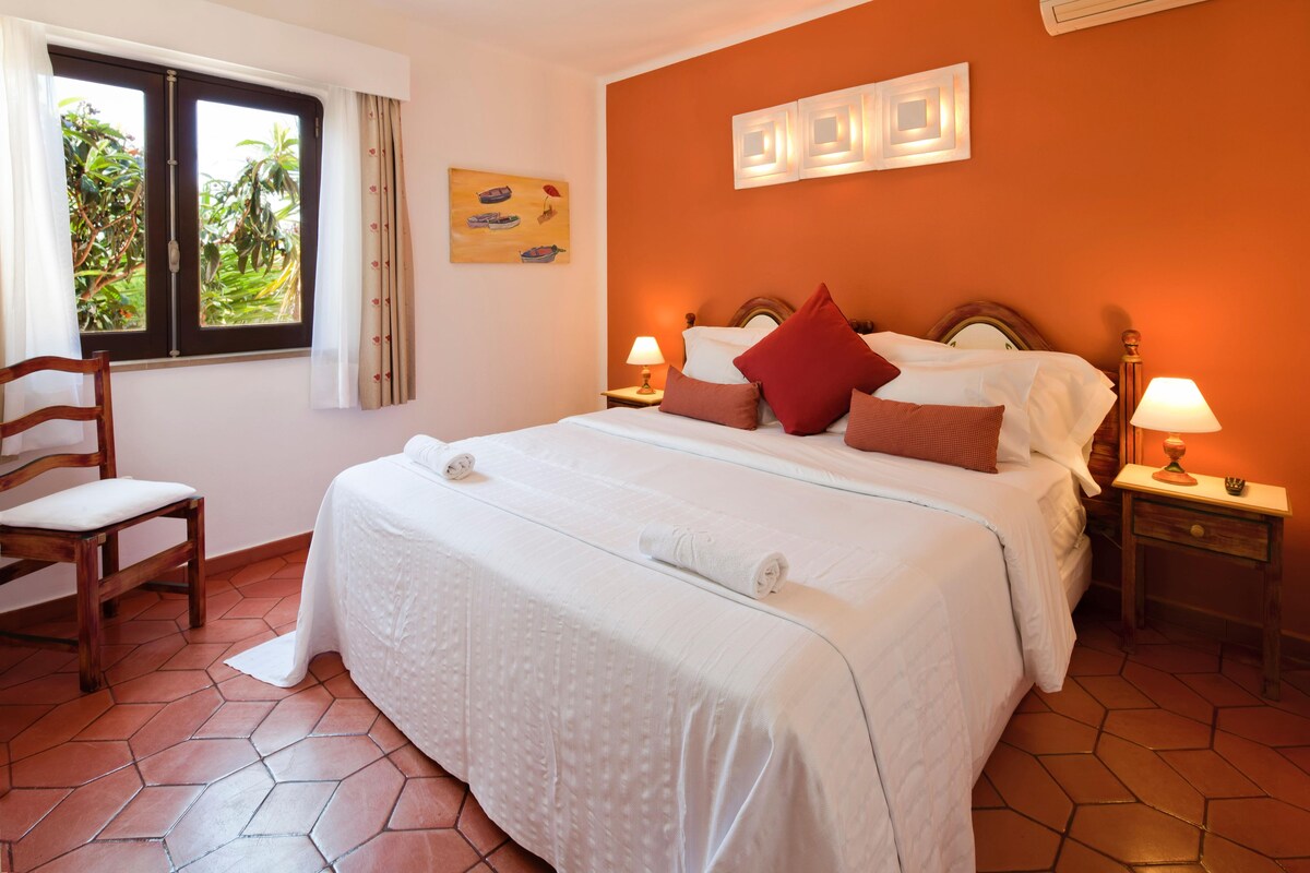 A hotel room with a large bed, two bedside tables with lamps, a chair, and a window with curtains.