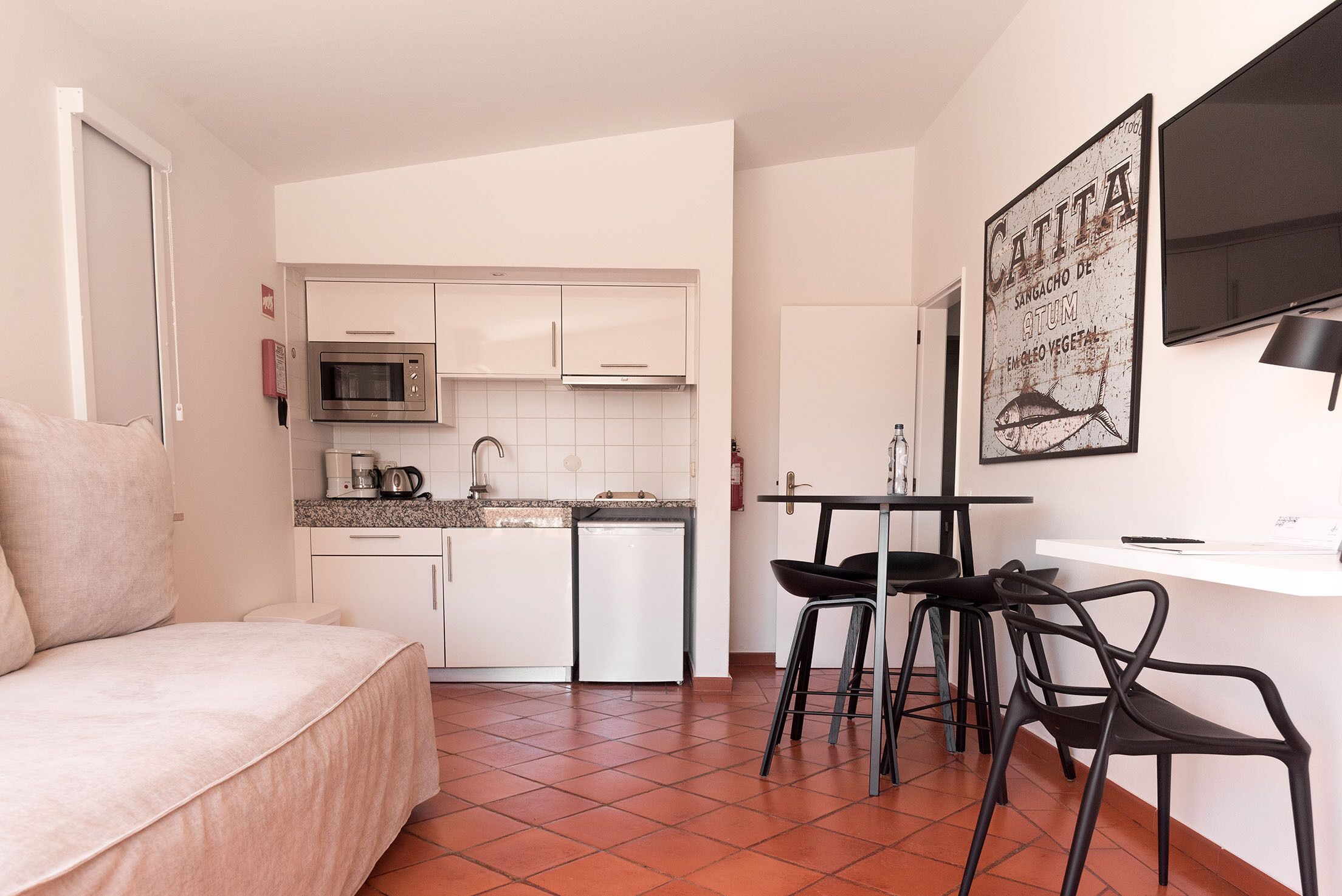 Un espacio habitable compacto con kitchenette, una zona de comedor con sillas y una cama.