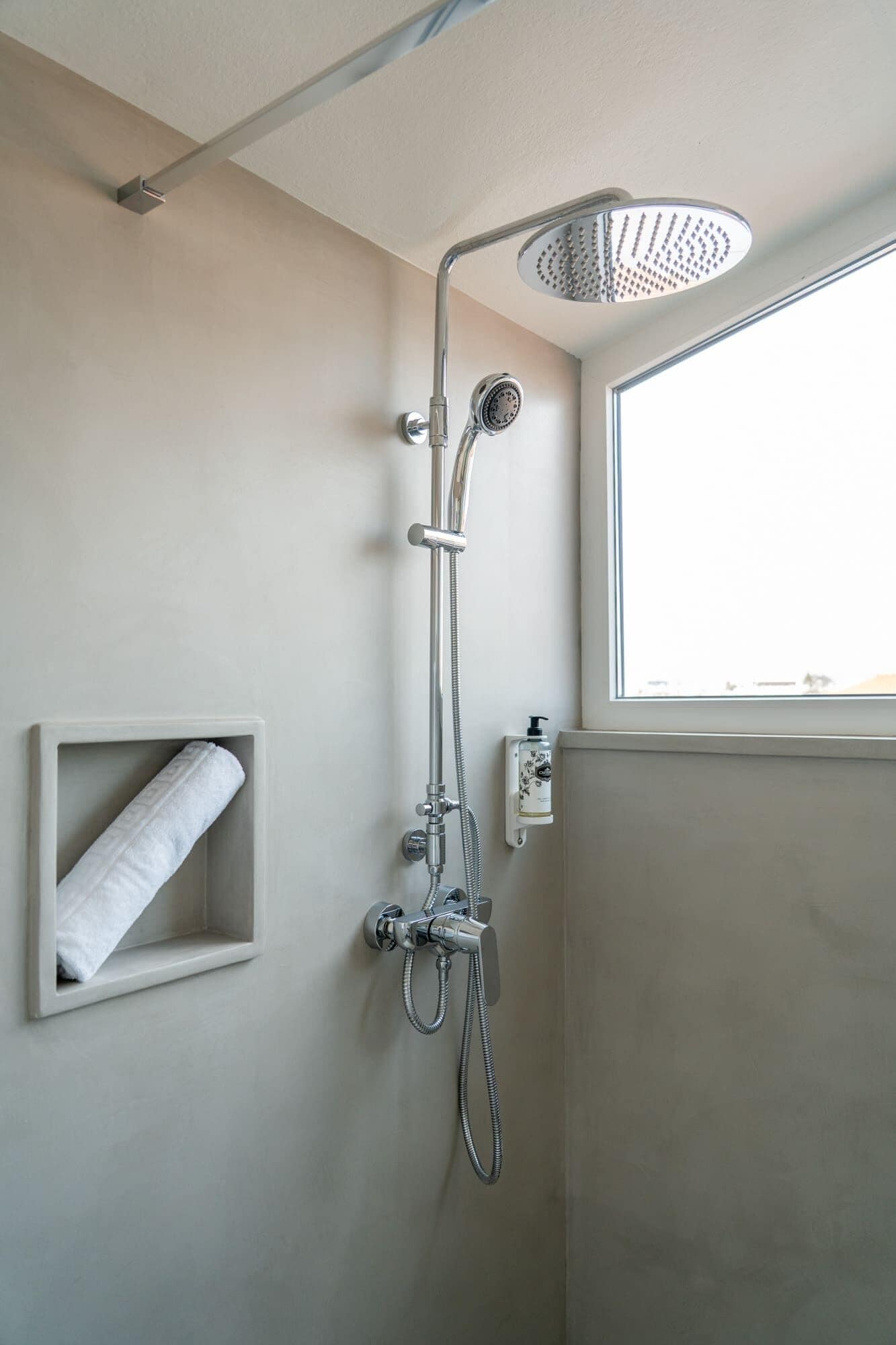 A modern shower with a handheld showerhead and a wall-mounted faucet, a towel rack, and a window providing natural light.