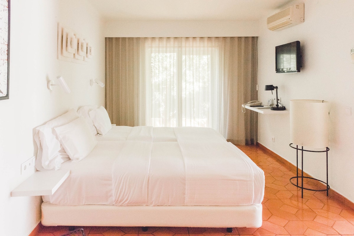A hotel room with a large bed, a desk with a telephone, a lamp, and a television on the wall.
