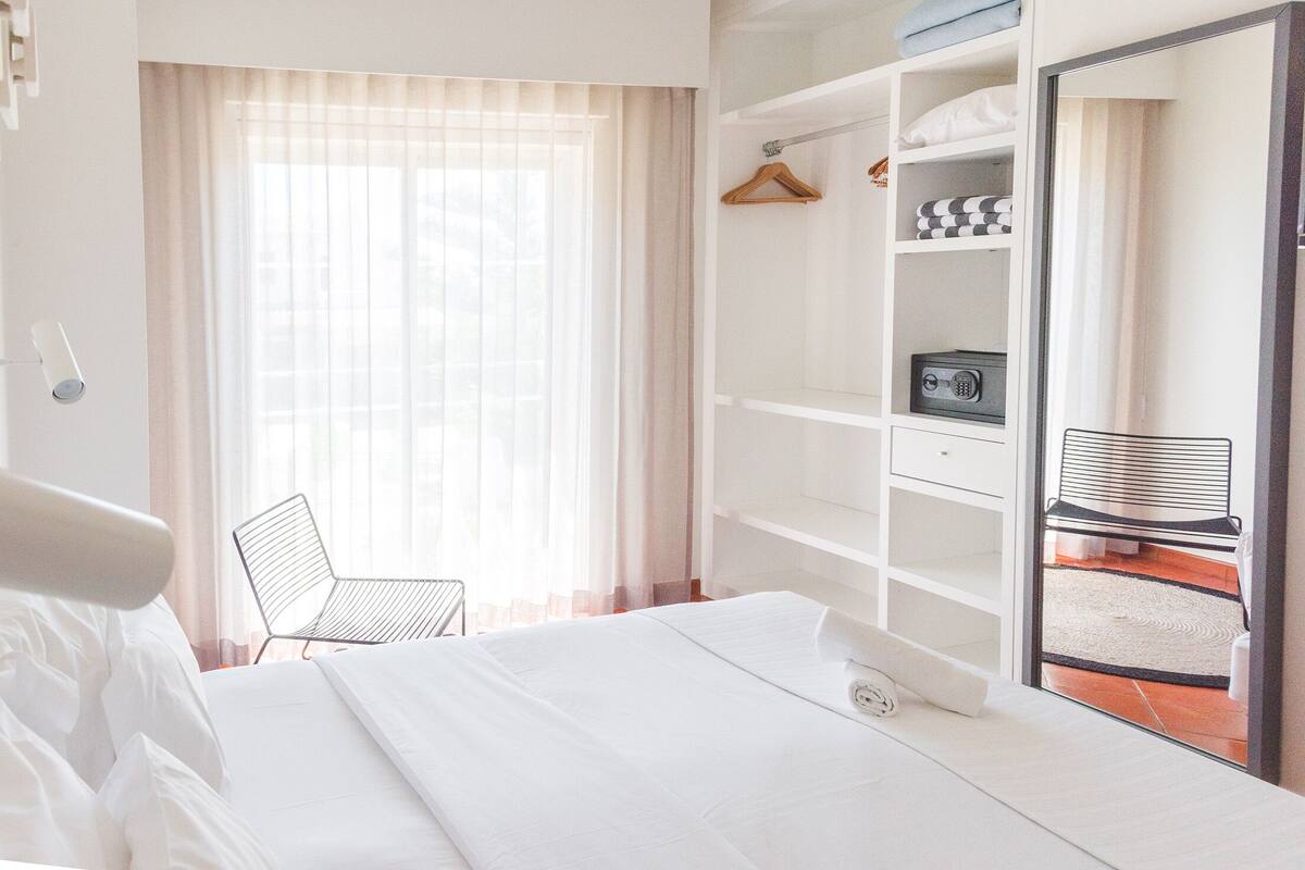 A hotel room with a bed, a chair, a wardrobe, and a mirror.