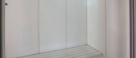 A white, minimalist bathroom with a built-in bench and a door.