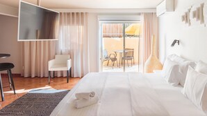 A hotel room with a bed, a TV, a chair, a table, and a view of the outside. - Costa D’Oiro Ambiance Village (Lagos)