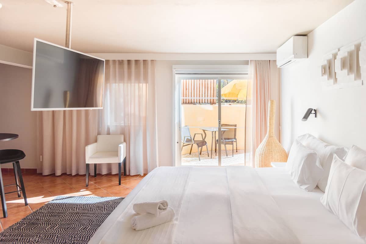 A hotel room with a bed, a TV, a chair, a table, and a view of the outside.