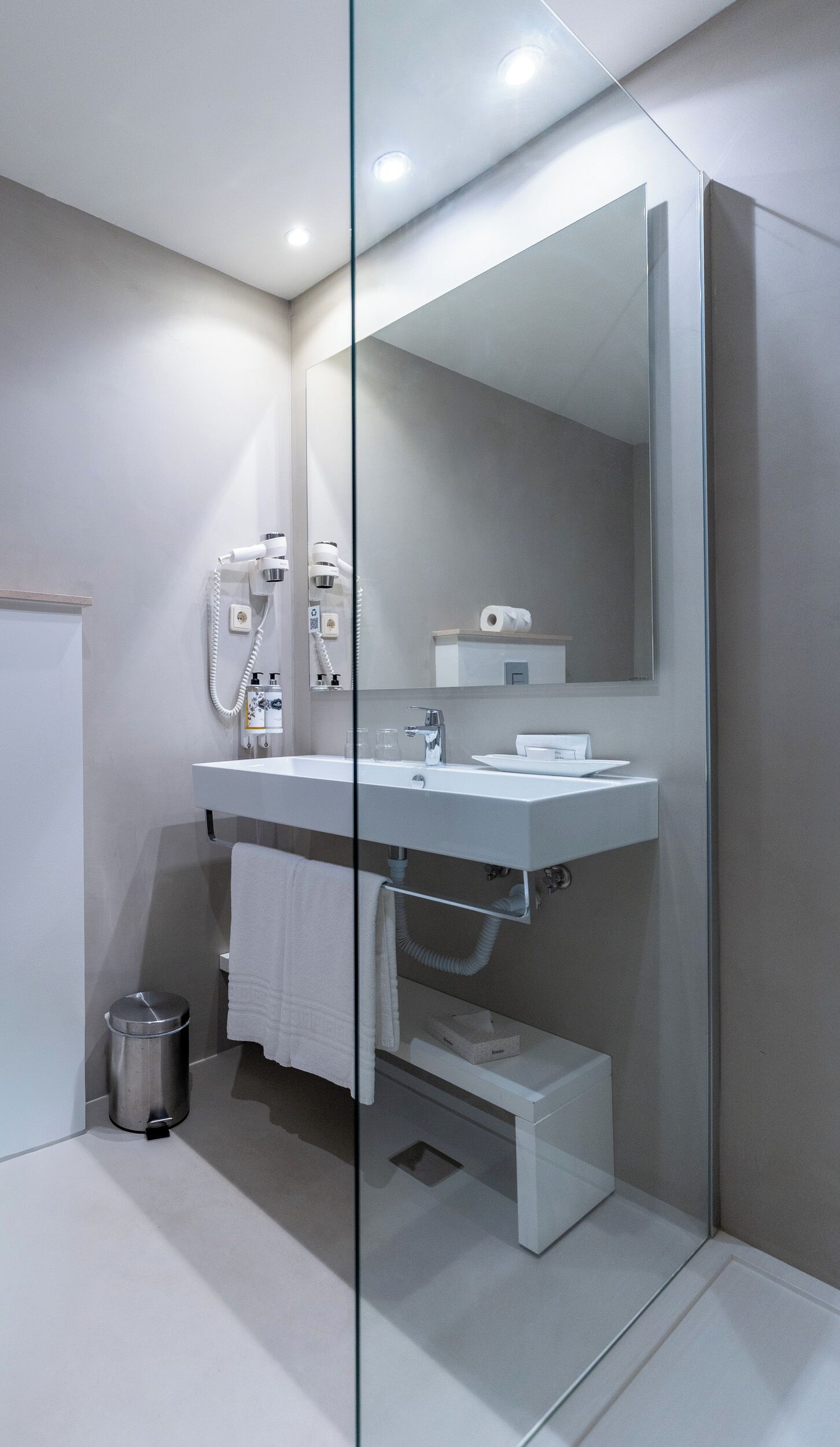 A modern bathroom with a glass partition, a white sink, a mirror, and a towel rack.