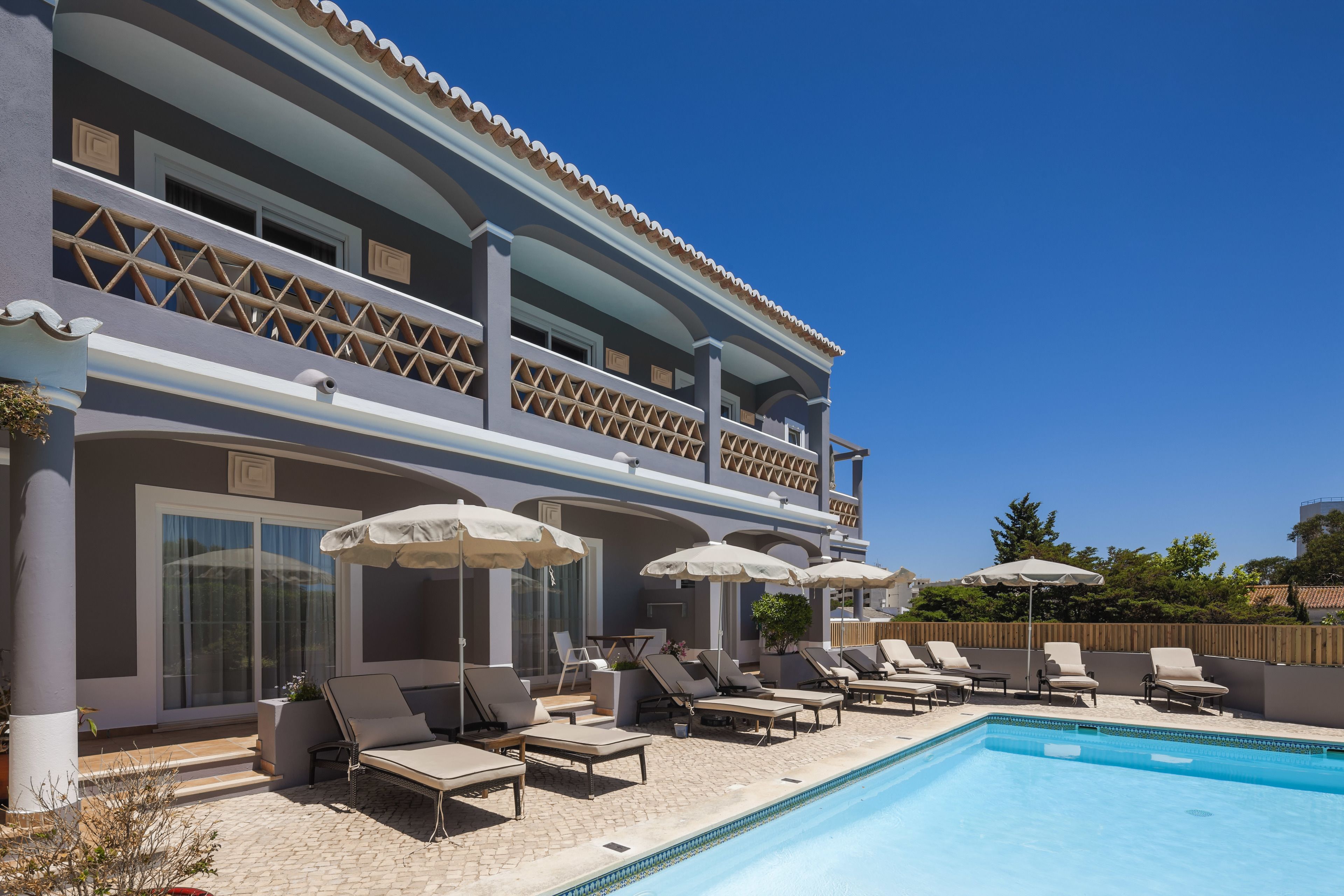 A two-story building with a swimming pool, sun loungers, and umbrellas.