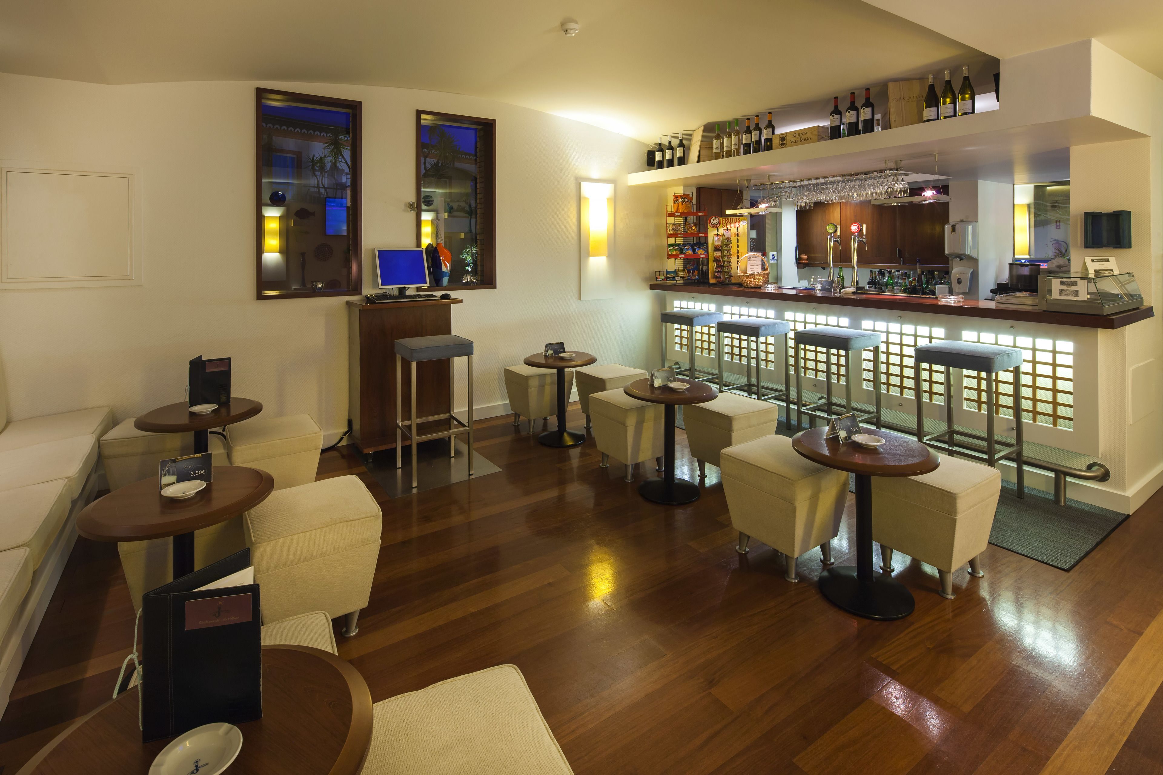 A modern bar area with a wooden bar counter, multiple stools, and a variety of bottles and glasses.