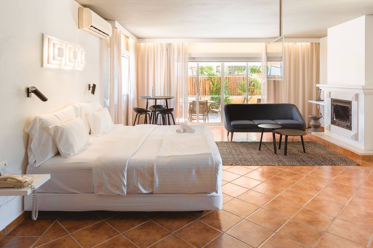 A hotel room with a bed, a small table with chairs, a sofa, a fireplace, and a view of the outdoors.