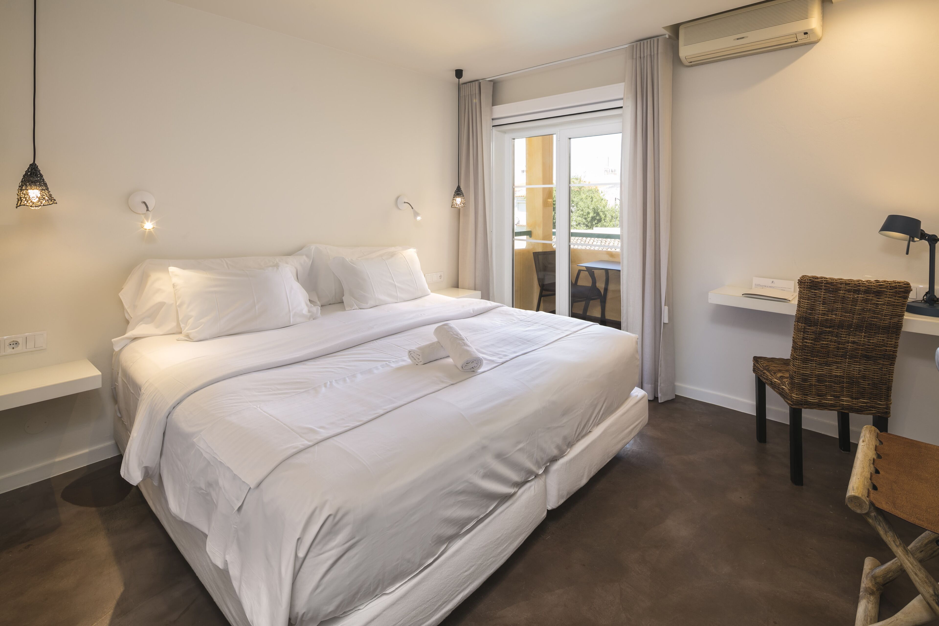 A modern hotel room with a large bed, a desk, and a view of the outdoors.