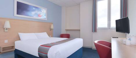 A hotel room with a bed, a desk with a chair, a TV, and a window with curtains.