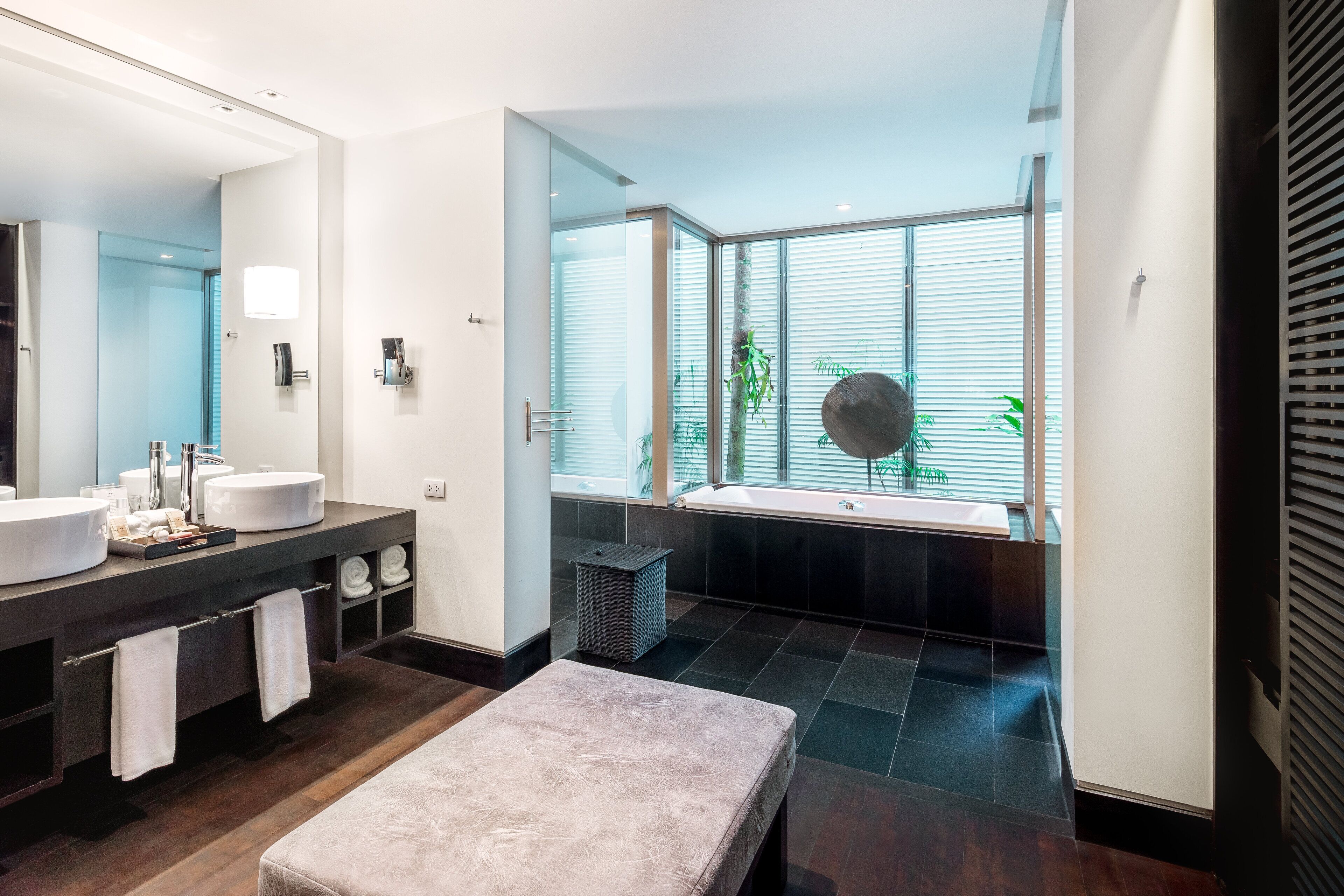 A modern bathroom with a large mirror, two sinks, a bathtub, and a bench.