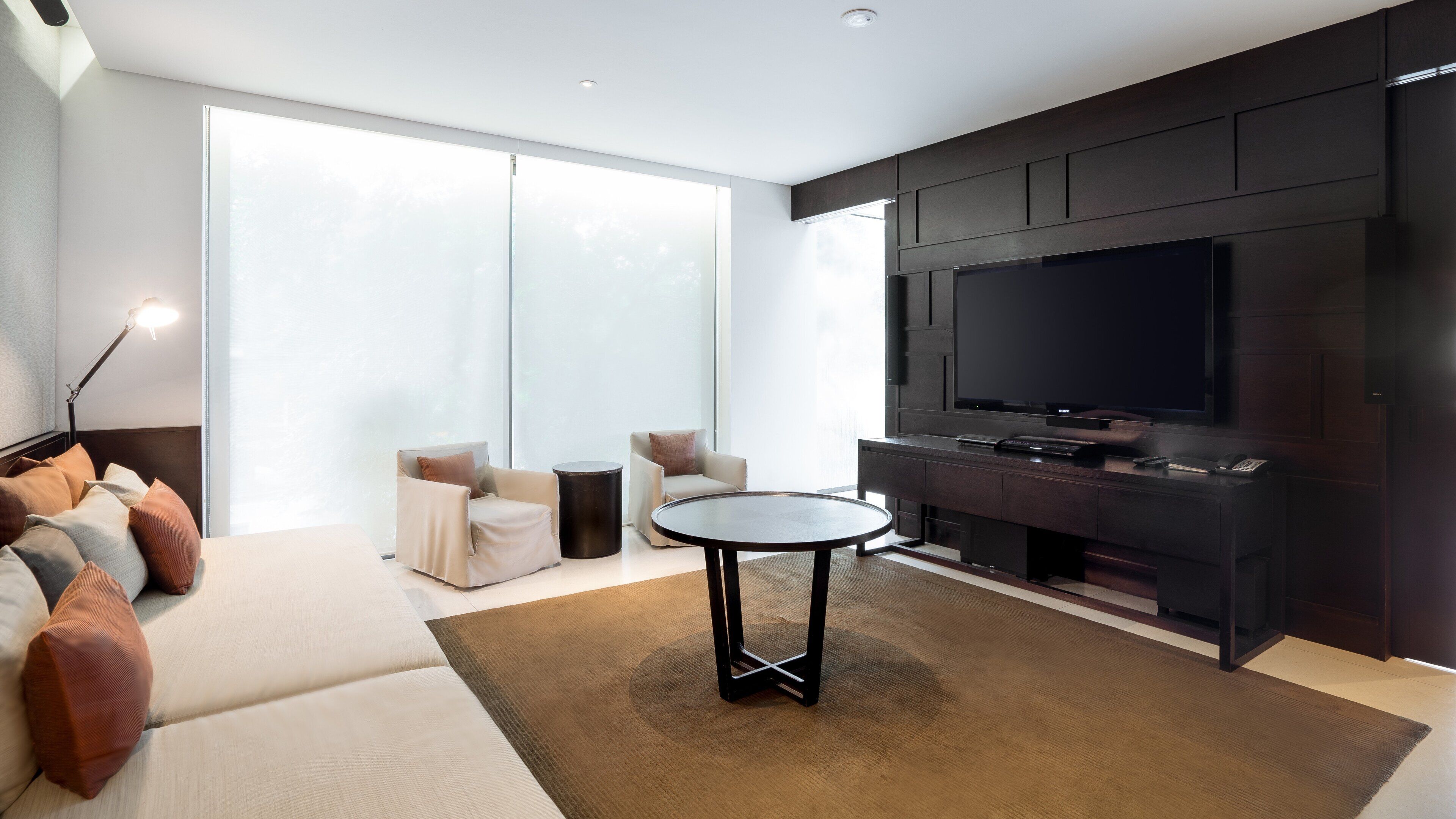 A modern living room with a large flat-screen TV, a sofa, two armchairs, a coffee table, and a floor lamp.