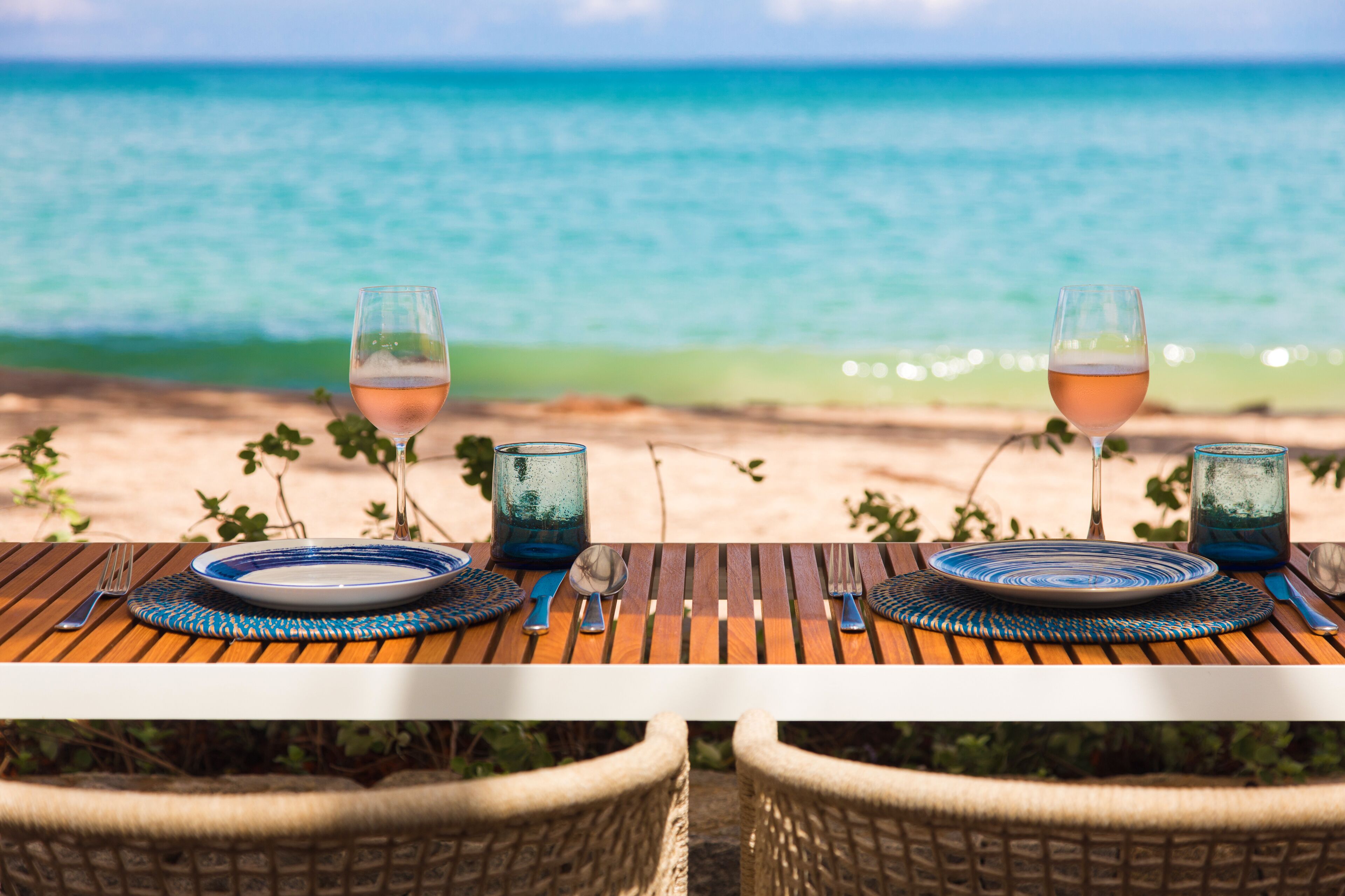 A table set with plates, cutlery, and glasses on a wooden table with a view of the ocean.