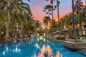A pool area with palm trees, lounge chairs, and a building with a wooden facade. - Twinpalms Surin Beach Phuket (Choeng Thale)