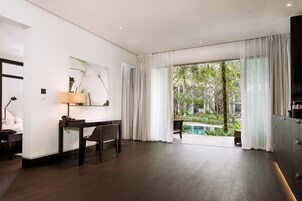 A modern hotel room with a wooden floor, a desk with a lamp, a chair, and a large window with sheer curtains.