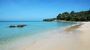 Una playa con agua turquesa cristalina, una orilla de arena y un promontorio boscoso al fondo.
