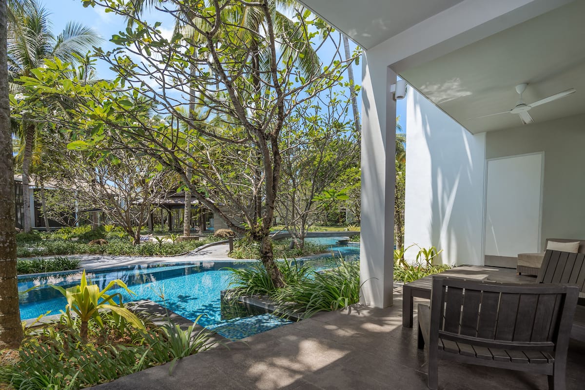 Un espace piscine offrant une vue sur un paysage arboré, une terrasse avec une table et des chaises, et un ventilateur de plafond.