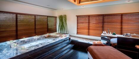 Une salle de spa moderne dotée d’une grande baignoire, d’une table de massage et d’une fenêtre avec des stores en bois.