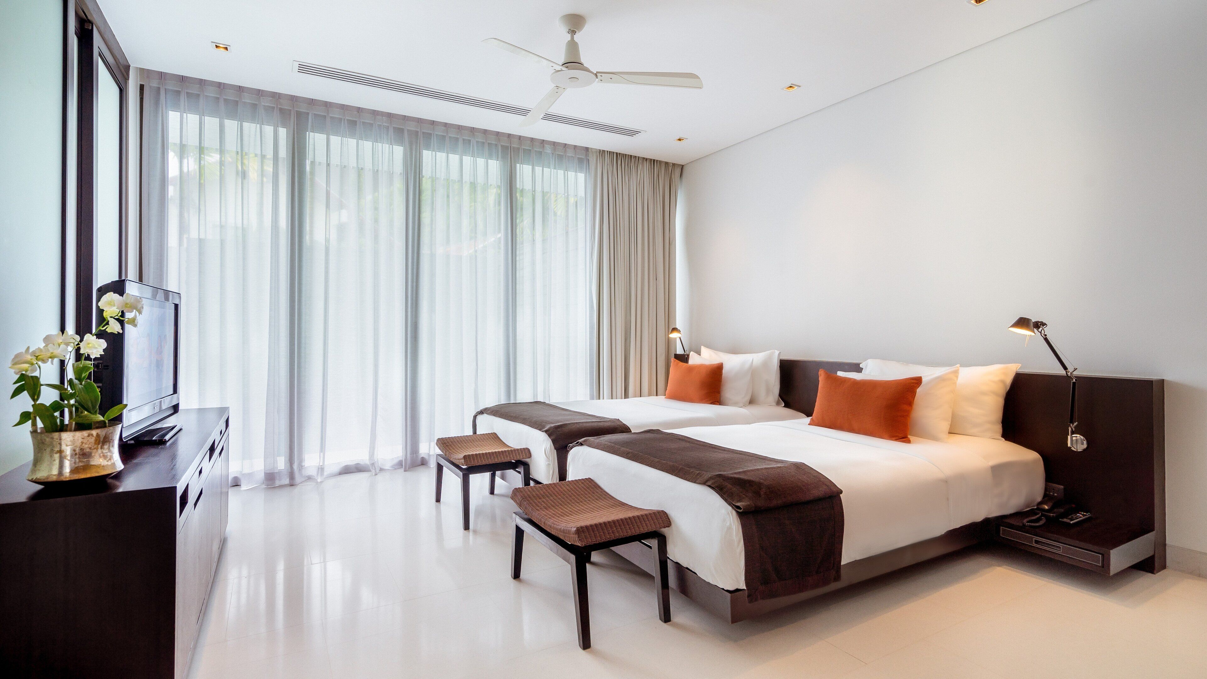 A modern hotel room with a large bed, two bedside tables, a desk with a TV, and a ceiling fan.