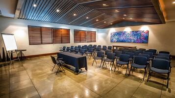 A conference room with a long table, rows of chairs, a whiteboard, and a large abstract painting on the wall.