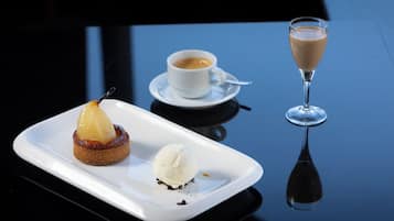 Ein Dessertteller mit Birnenstrudel und Eis, eine Tasse Kaffee sowie ein Glas Champagner auf einem dunklen, spiegelnden Tisch.