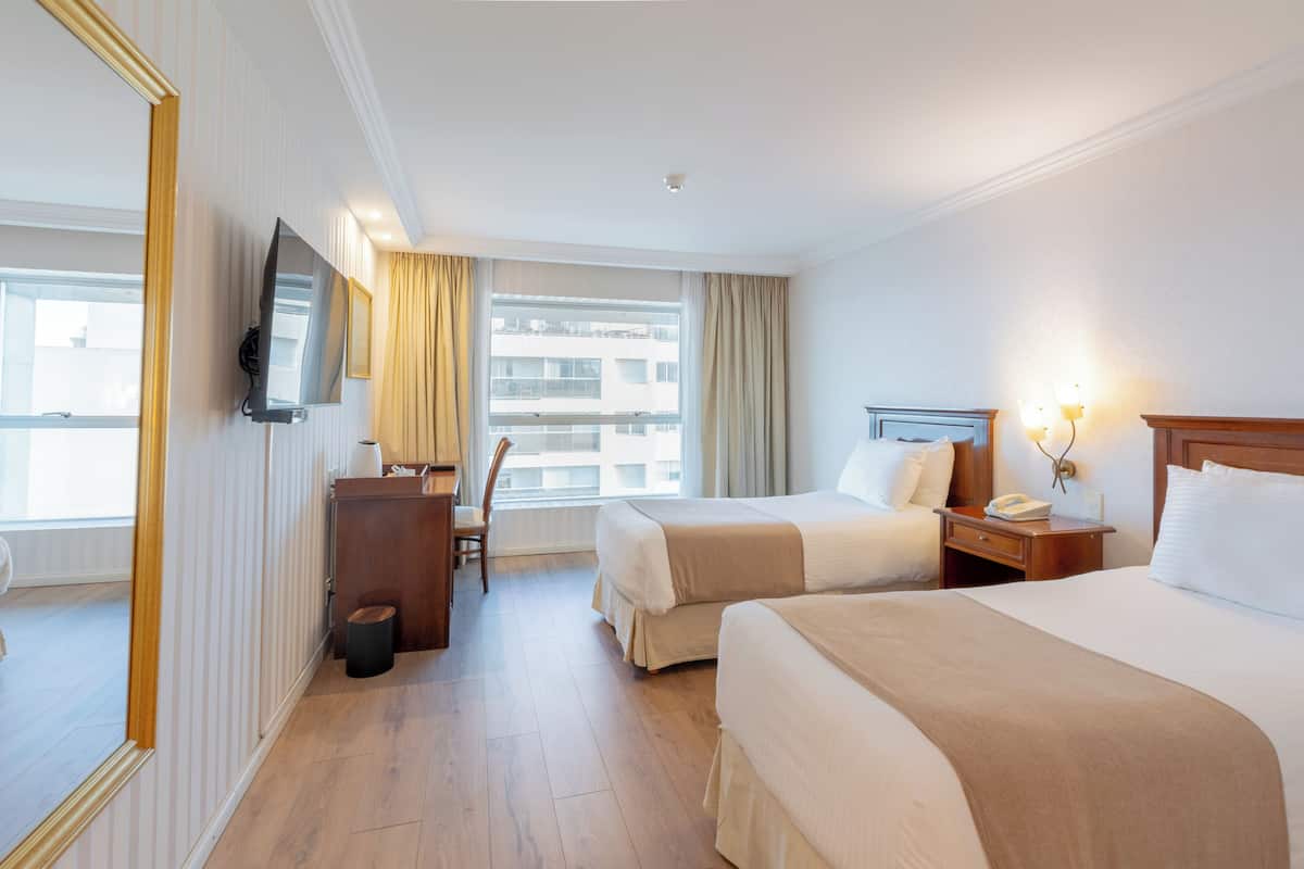 A hotel room with two beds, a desk, a chair, a TV, and a window with curtains.