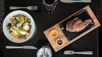 Una mesa de comedor con un bistec, ensalada y dos copas de vino tinto.